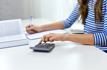 education, school and knowledge concept - close up of student girl counting on calculator and writing to notebook at home