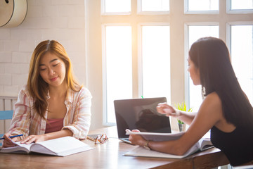 Two beautiful Asian students are using computers and textbooks. Review lesson at home With warm light