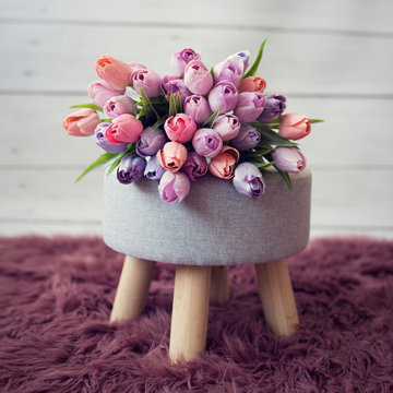 Bouquet of tulip flowers. Natural sprin flower decoration. Violet, purple, orange and pink tulips on grey tabouret.