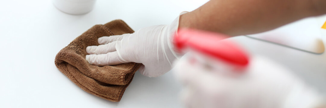 Focus on gloved male hand holding doormat and swiping dust inhabited by harmful bacteria from white workplace with concentration and diligence. Pleasant clean-up concept. Blurred background