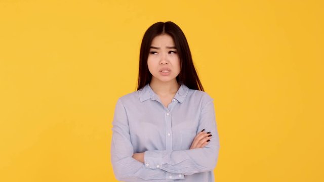 Pensive Asian girl on yellow background, idea concept