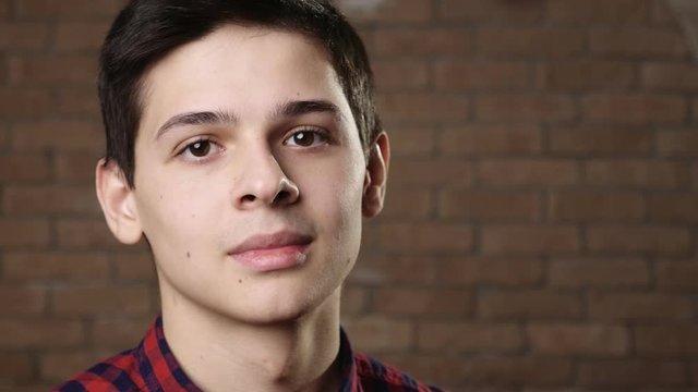 Dreamy young man in a checkered shirt tittering and smiling in a brick studio