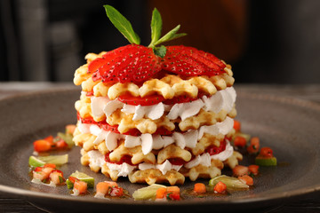 Multilayer waffle cake with ripe strawberries and whipped cream, garnished with mint and strawberries, with sauce of finely chopped strawberries, mint and lime. Close-up on a plate.