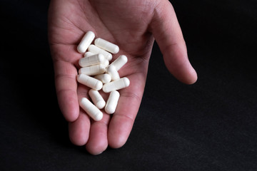 White pills on hand on black background. Antibiotic capsule pills. Medicine pill.