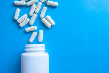 White capsule pills with bottle on blue background. Drugs narcotic concept. Healthcare concept. Capsule pharmacy bottle pill drug concept.