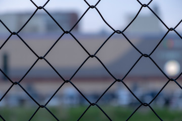 Fototapeta premium Chain link fence on a blurred city background. Metall wire fence with unfocused city backgorund.
