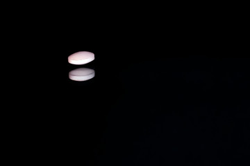 Pink pill with reflection on black background. Pharmacy background. Drug concept.
