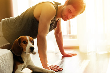 Smiling bearded man doing exercises push ups against the window at home with his dog