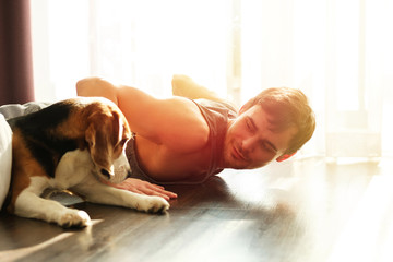 Smiling bearded man doing exercises push ups against the window at home with his dog