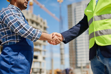 Two male engineers shake each others hands friendly.