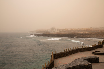 Calima weather with low visibility towards San Blas and Golf del Sur, popular southern resorts in Tenerife, as seen from the harbor promenade in the small village of Los Abrigos, Canary Islands, Spain