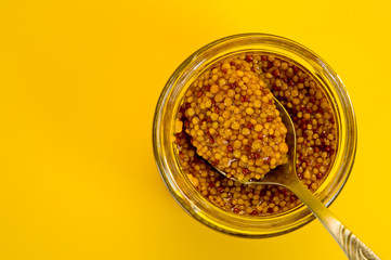 French mustard in a glass jar, shot on a yellow background. Background for seasoning and nutrition.