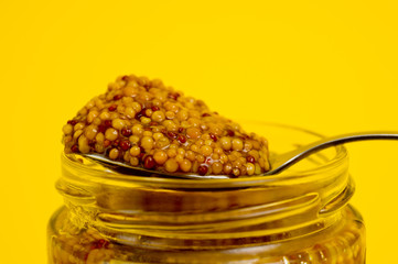 French mustard in a glass jar, shot on a yellow background. Background for seasoning and nutrition.