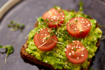 food, eating and breakfast concept - toast bread with mashed avocado, cherry tomatoes and greens on ceramic plate