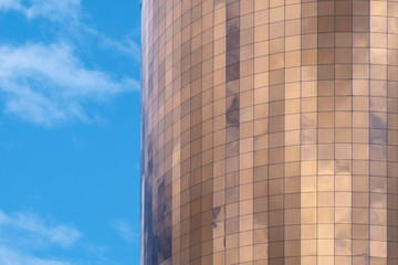 Obraz premium Facade of cylynder form scyskraper with golden mirror glass on a blue sky background.