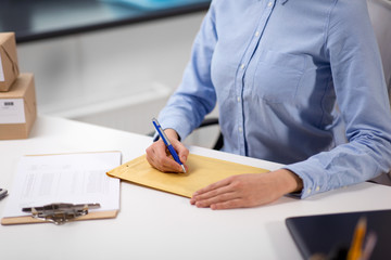 delivery, mail service, people and shipment concept - close up of woman with pen writing address on...