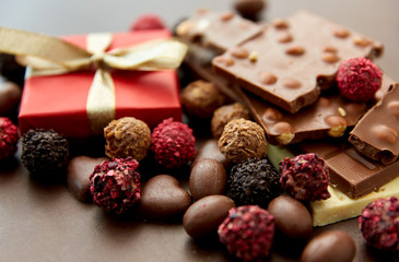 sweets, confectionery and food concept - close up of different chocolate bars, candies and gift box on brown background