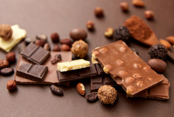 sweets and food concept - milk, dark and white chocolate bars with nuts, candies, cocoa beans and powder on brown background