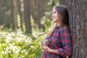 Asian girl with an old camera in a forest. Girl in checkered shirt and blue jeans taking photo on an old camera. Vintage style...