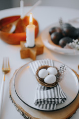 Easter table setting with white plate, gray textile napkin, candles, quail and chicken eggs and blossom branch.Mock up easter card