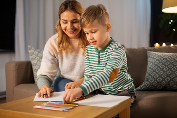 family, leisure and people concept - mother and little son with colored pencils and paper draw at home