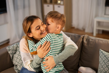 family, love and people concept - happy smiling mother and little son hugging and kissing at home...