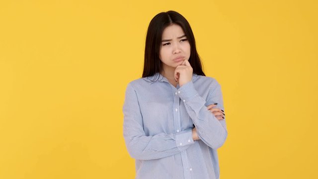 Pensive Asian girl on yellow background, idea concept