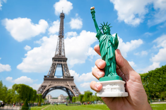Hand of an unrecognizable American tourist holding a souvenir Statue of Liberty in front of the Eiffel Tower in Paris, France