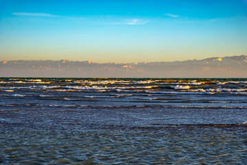 Big waves on the sea on a windy day on evening with mountains silhouettes on background.