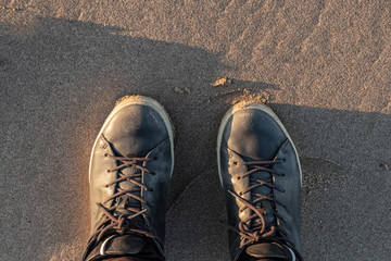 Human in black leather shoes on a wet sand, top view.