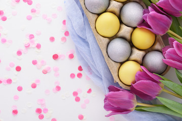festive Easter composition of purple tulips and yellow and blue Easter eggs with pink confetti on white background