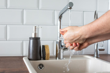 Hand washing underwater from a faucet in the kitchen close-up. leanliness, water saving, washing dishes in a bright Scandinavian interior