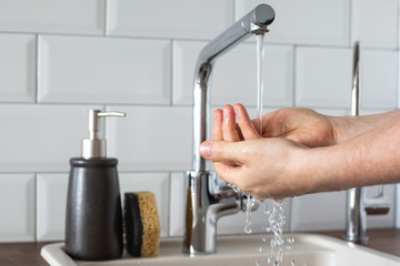 Hand washing underwater from a faucet in the kitchen close-up. leanliness, water saving, washing dishes in a bright Scandinavian interior