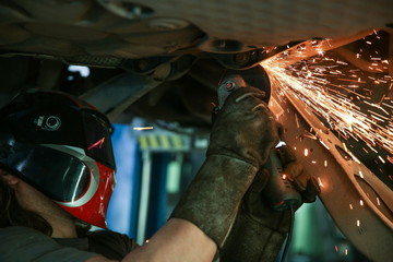 mechanic cuts a rusty bolt in a car with an angle grinder