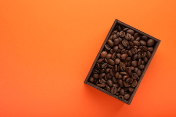 roasted coffee beans in a wooden box on orange background flat lay with copy space