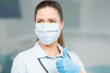 female doctor with medical face mask and medical gloves shows thumbs up 