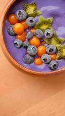 Smoothies of violet color from banana and currant, on top of a blackberry, physalis and kiwi berry. Smoothies in a wooden bowl.