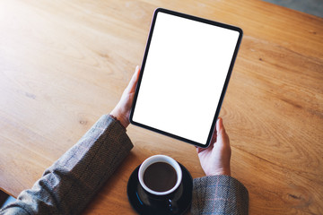 Top view mockup image of a woman holding black tablet pc with blank white screen with coffee cup on the table