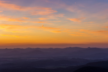 Clearly bright sunset. Orange clouds above sunset. Silhouette of rocks in the front.