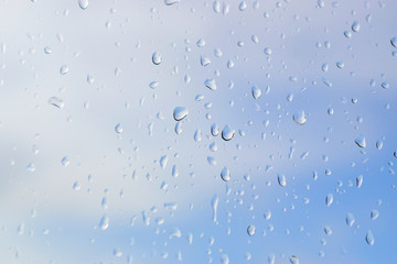 Abstract blurred of water drops or raindrops on the glass of window over blur sky used for background.