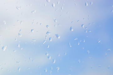 Abstract blurred of water drops or raindrops on the glass of window over blur sky used for background.