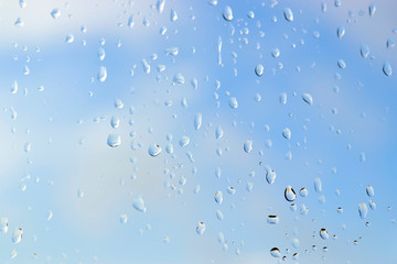 Abstract blurred of water drops or raindrops on the glass of window over blur sky used for background.