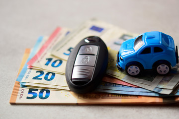 Macro shooting of key car with blurry car over blurred banknotes on blurry gray background. Car...