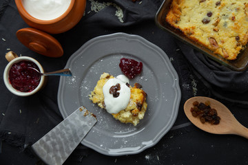 Cottage cheese casserole with raisins on a gray plate, poured sour cream on top. Flat lay, view from above. 