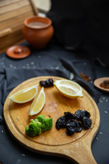Ingredients for cooking. Products on a round wooden board: lemon slices, prunes, broccoli and dried grapes (raisins) in a wooden spoon. 