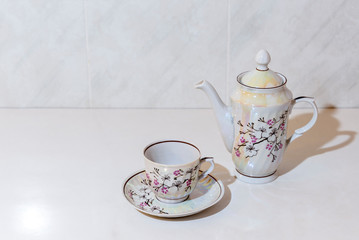 Cup of coffee and coffee pot on a white table lit by the morning sun