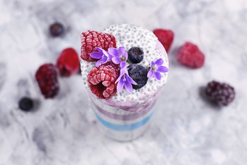 Layered smoothie with natural colored fruit and healthy chia seed pudding in drinking glass decorated with flowers