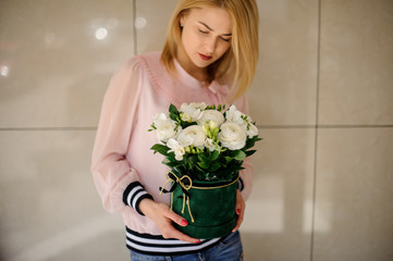 Beautiful woman holding flower composition in round box and looks at it.