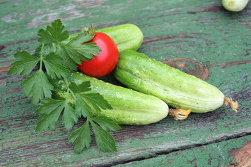 Organic green cucumbers and tomato on the background of boards