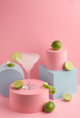 Glass of Margarita cocktail and fresh limes on pink background